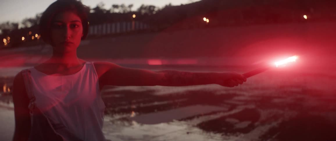 A woman holding a lit red flare with houses and trees in the background