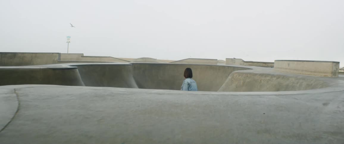 A teenage girl rides a skateboard into a skate bowl at a park