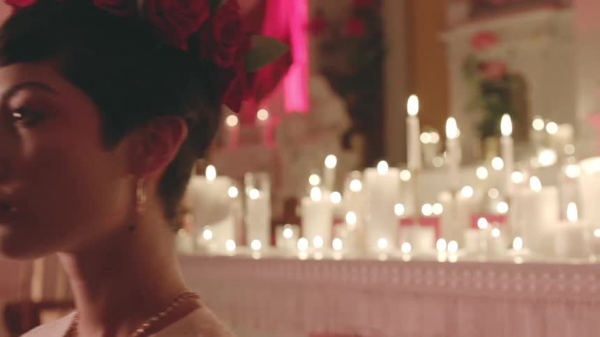 A woman stands in front of a table with burning candles and then walks away