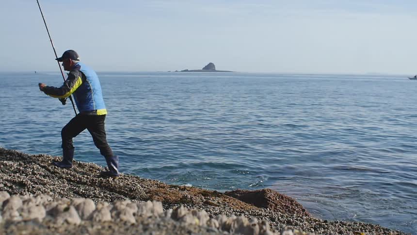 An older man carrying a fishing pole walking away from the shore