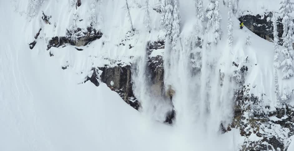 A skier throws snow down over a huge cliff