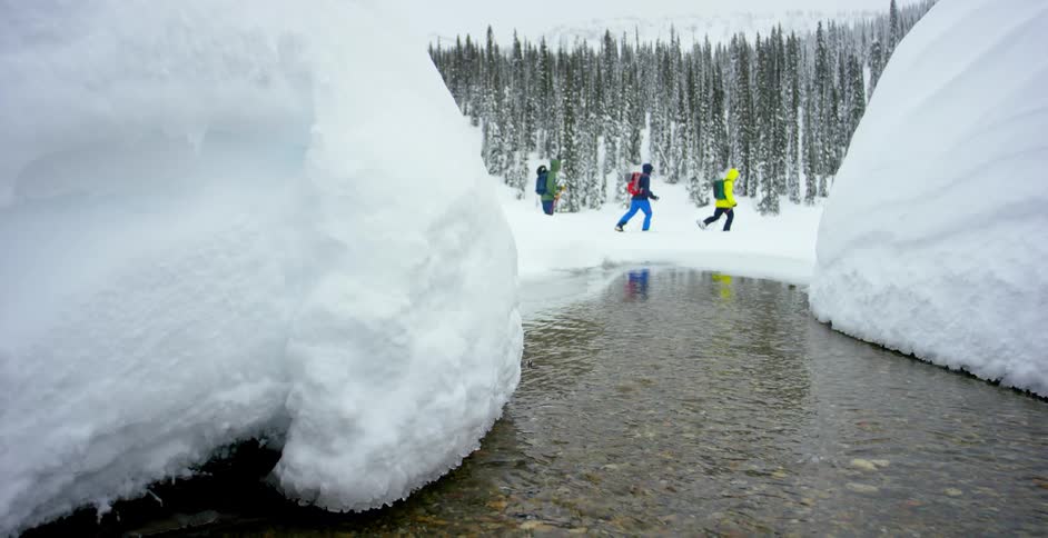 Three people ski through the snow past a stream