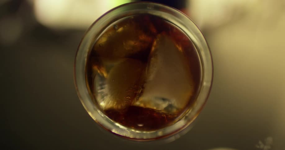 A brown liquid pours into a glass filled with ice