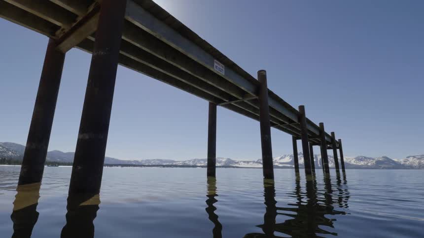 The sun shining down on a mountain lake, pier and snow-capped mountains