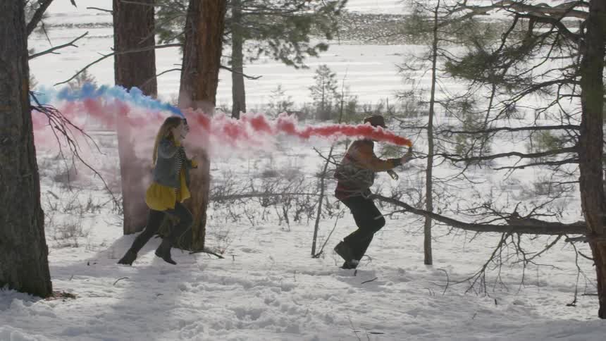 A man and woman holding smoke bombs run in the snow