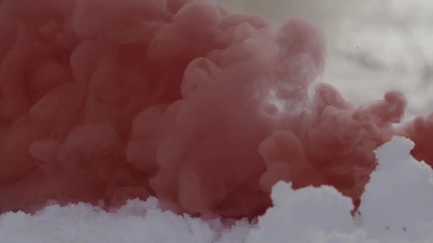 A red billowing smoke moves over a snowy landscape