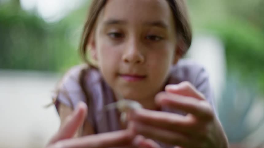 A young girl holds a snail in her hands and looks at it