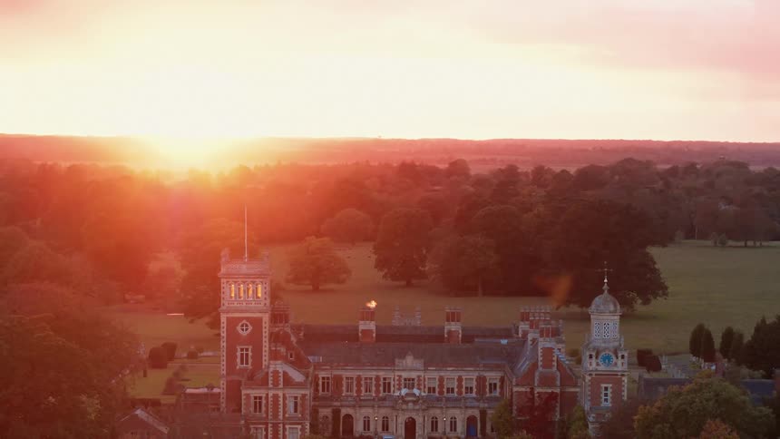 Sun sits on horizon turning sky red near large estate surrounded by trees