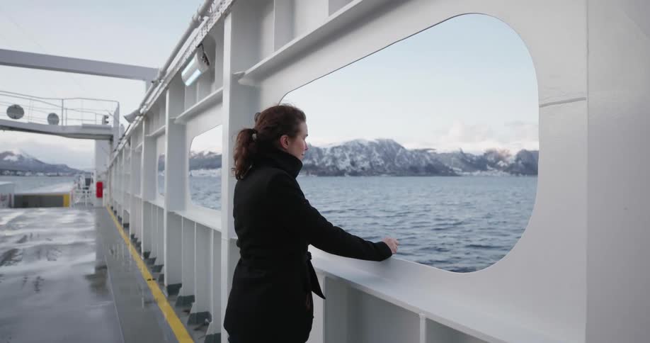 Woman stands in a large boat as it travels in the ocean near the mountains