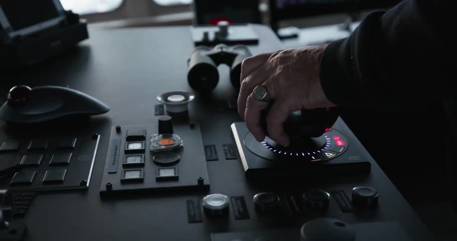 A white man piloting a ship has his hand on the control
