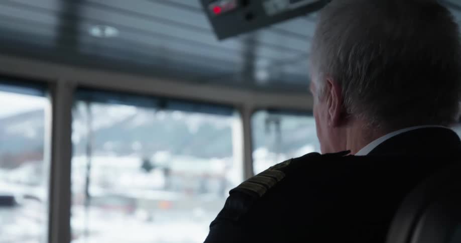 A captain of a ship sits in the bridge of a ship looking out a window
