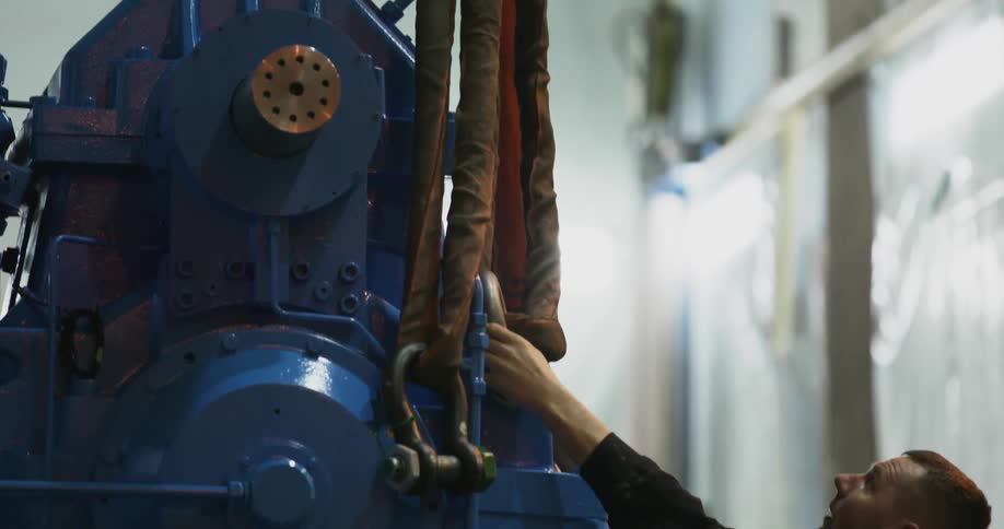 A white male employee of a factory works on a large piece of machinery