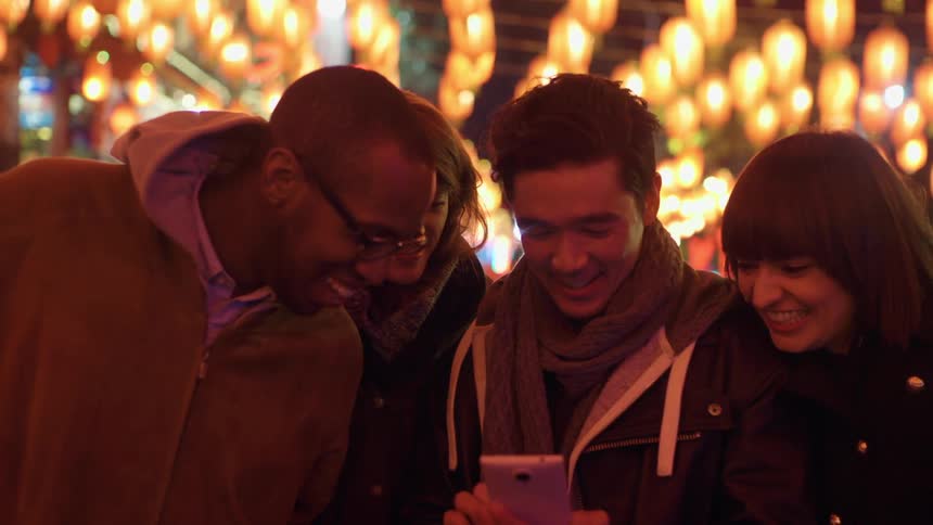 A small group huddles around a smartphone smiling and laughing
