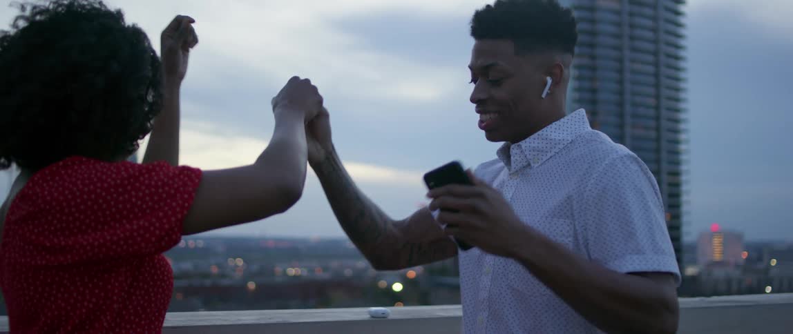 Black man and woman dance on the rooftop of a building at dusk