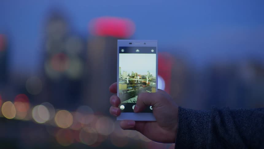 A woman takes photos of Beijing at blue hour with his cell phone