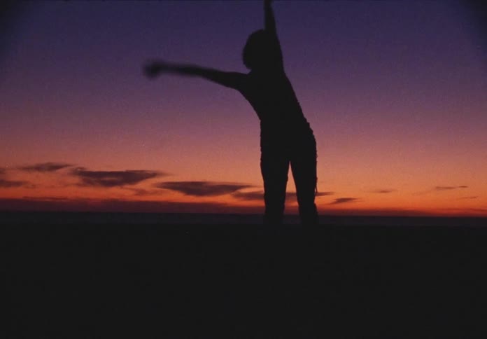 A young woman dances in silhouette outdoors at dusk