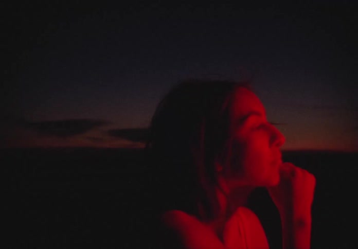 Woman in red light dances on the beach at dusk