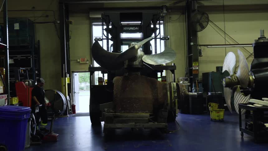 A worker in a warehouse moves a large machine with boring blades on it while another watches