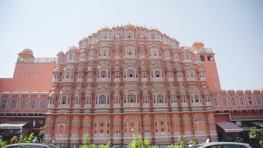 People and traffic pass by an ornate pink building in a developing country