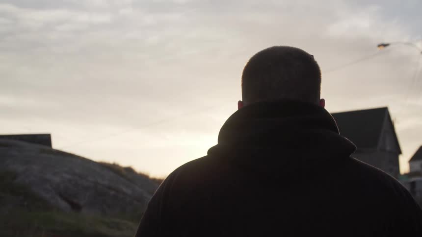 A white man walks while carrying a drone in a rural area