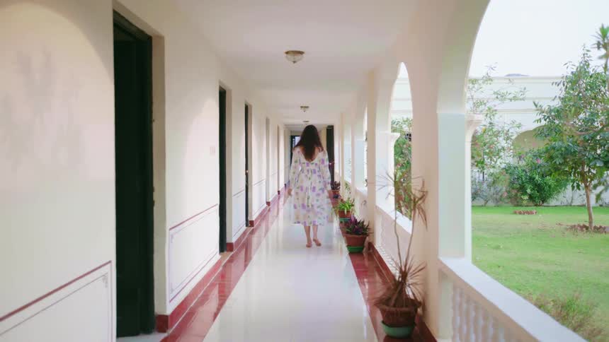 Woman in a floral dress slowly walking down an open hallway