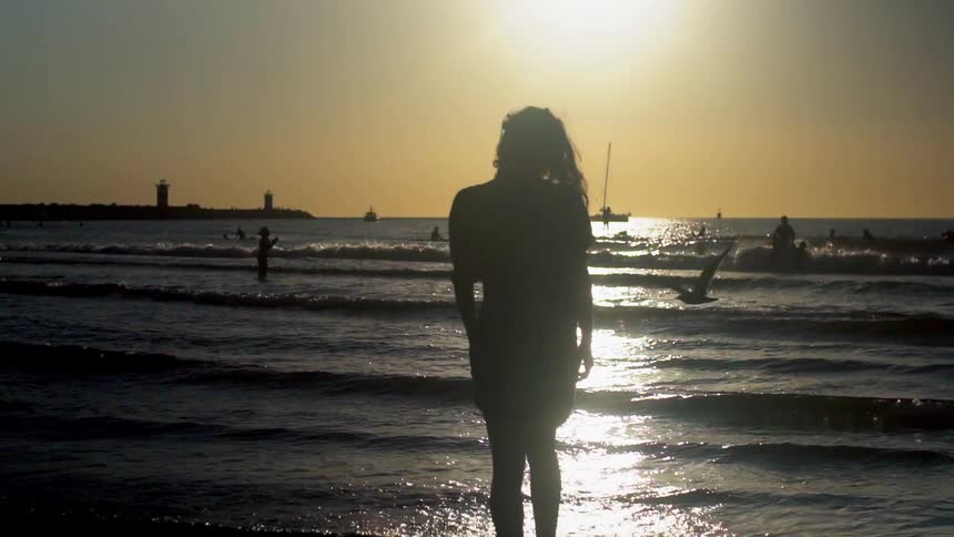 A woman in a dress walks into the tide at the beach