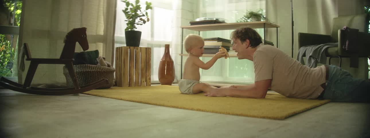 A father lies on the floor in his house and plays with his baby