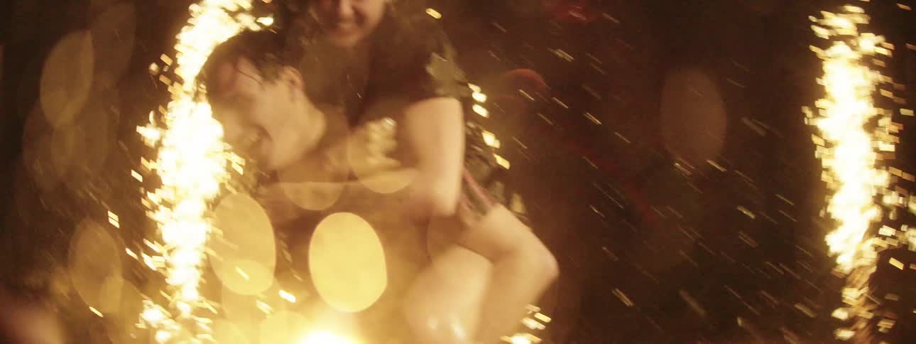 Three teens play in the water outside at night while flares throw sparks in the air