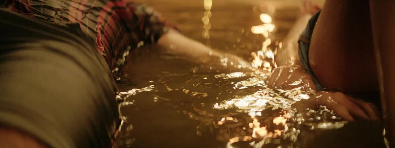 A man reaches for his girlfriends hand as they lie in a shallow puddle of water