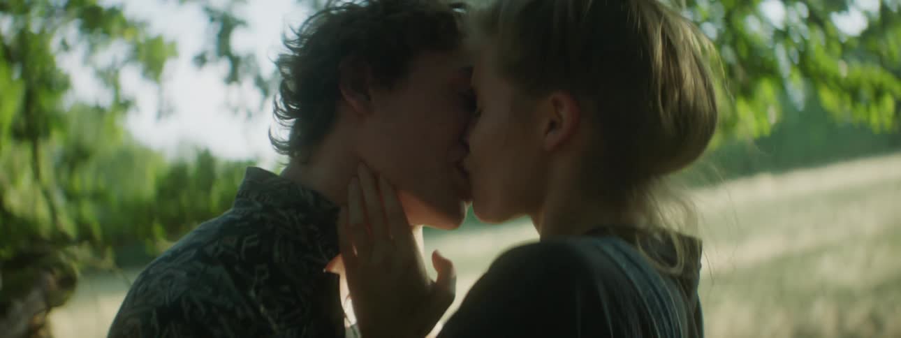 Two teens kiss outside under some trees