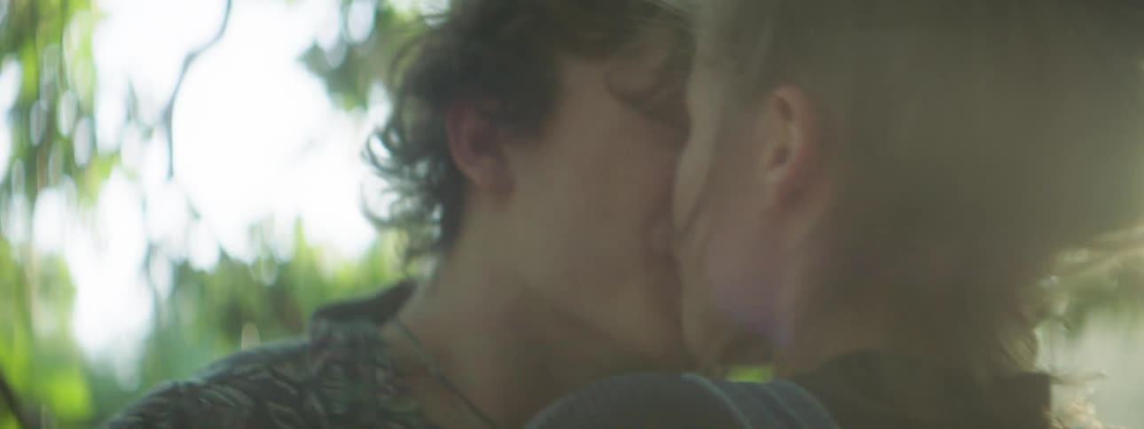 Two teenagers kiss while standing in the woods