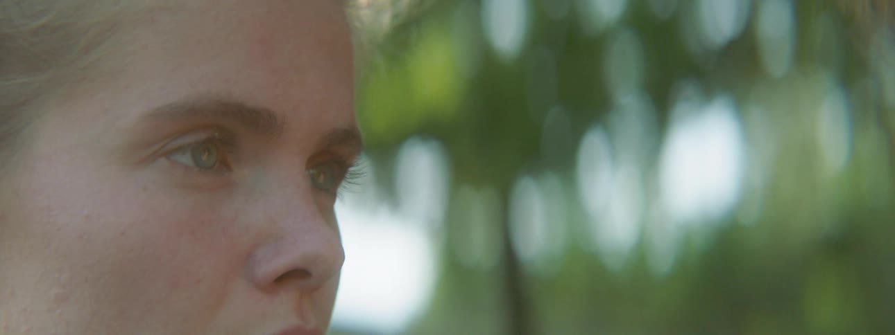 A white female teenager stands outdoors and thinks