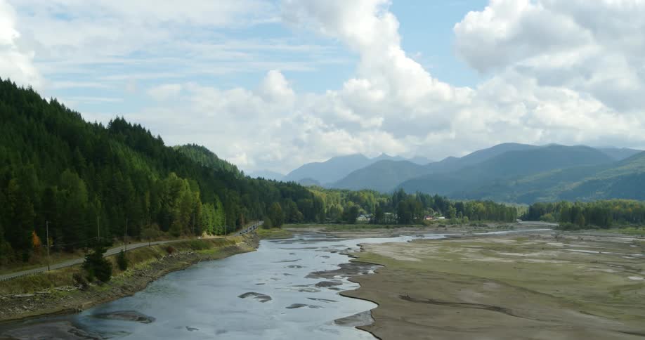 A car drives down a road next to a shallow river