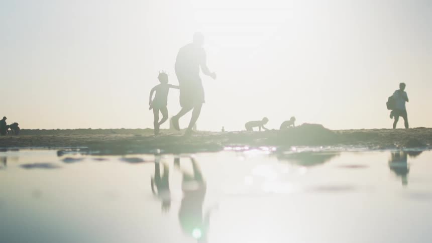 A silhouette of a father and daughter run on the beach