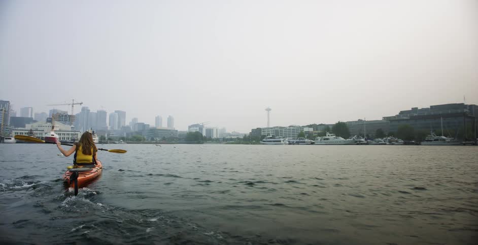 Woman rows kayak in the sea near waterfront city at sunset