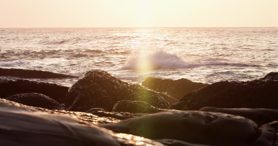 Sun light shines and glares on the ocean waves as the splash and break against the rocky shore