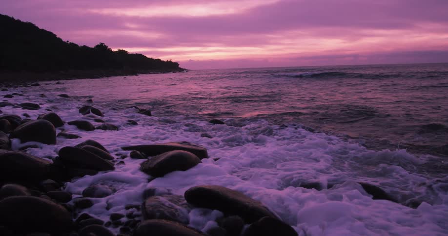 Ocean waves crash against the rocks at dusk