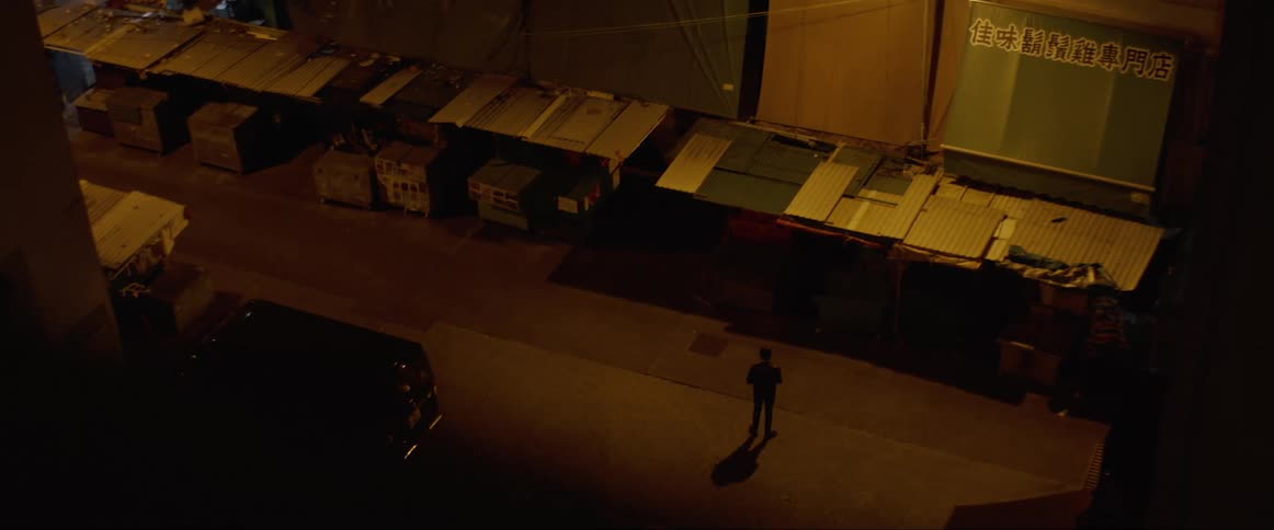 A man stands in a dark alley lined with trash receptacles
