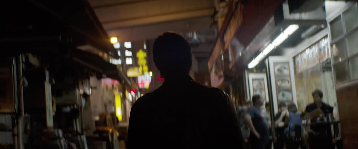 A man walks through an alleyway filled with people and stores
