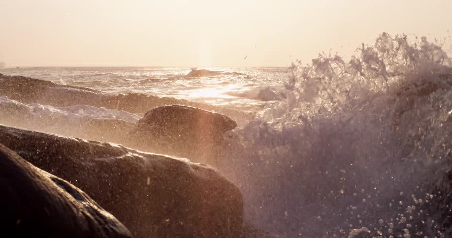 A huge wave crashes into a shoreline and covers big rocks with water