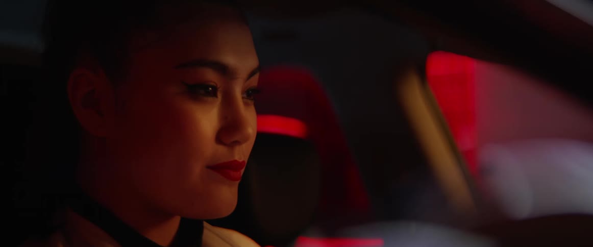 A woman sits in a car with a small smile on her face