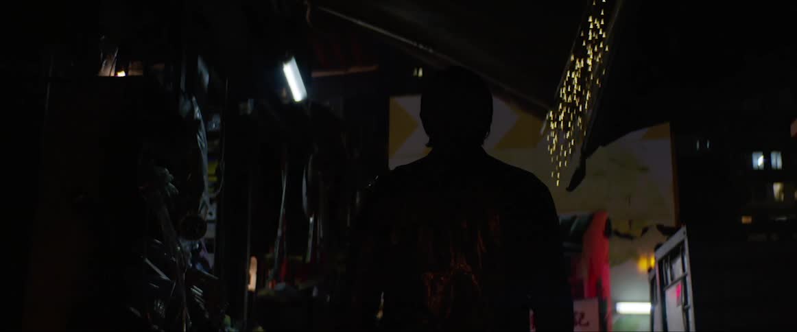 A man wearing a jacket walks through a cluttered hallway