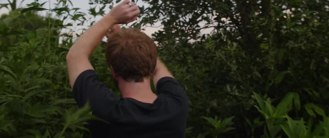 Three teens walk through tall weeds on a path