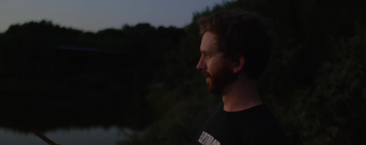 Man stands near still water and woods fishing