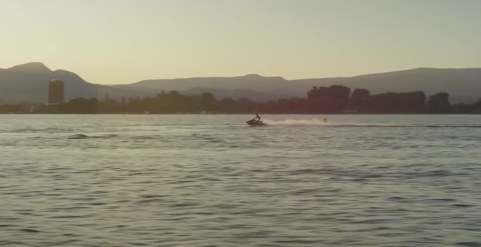 A person rides a jet ski through a lake and past a city skyline