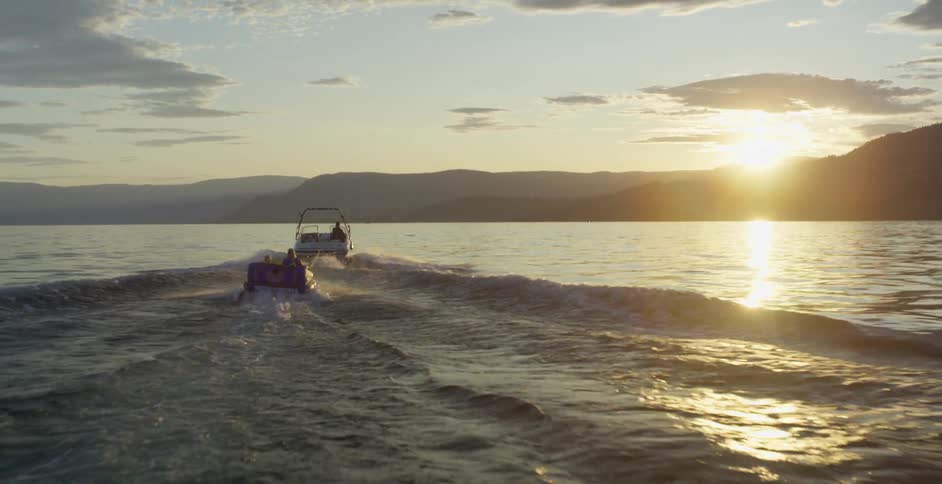 Boat towing kids on a raft in the lake at sunset