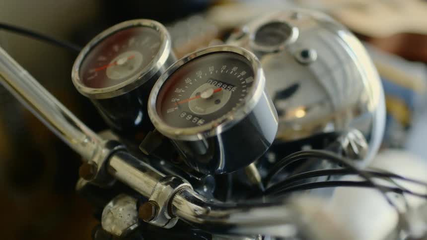 The gauges and handlebar of a motorbike as the chrome reflects images and light from the surroundings