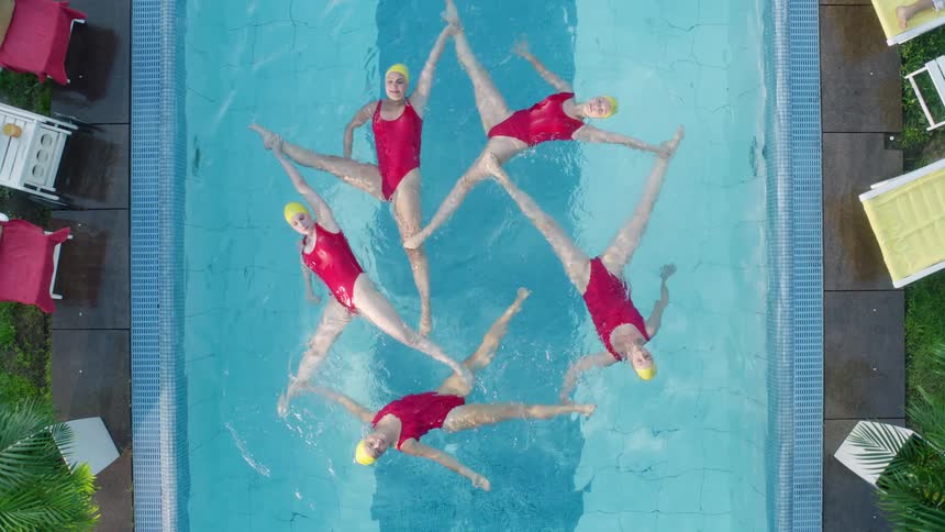 Five women perform a synchronized swimming routine in an outdoor swimming pool