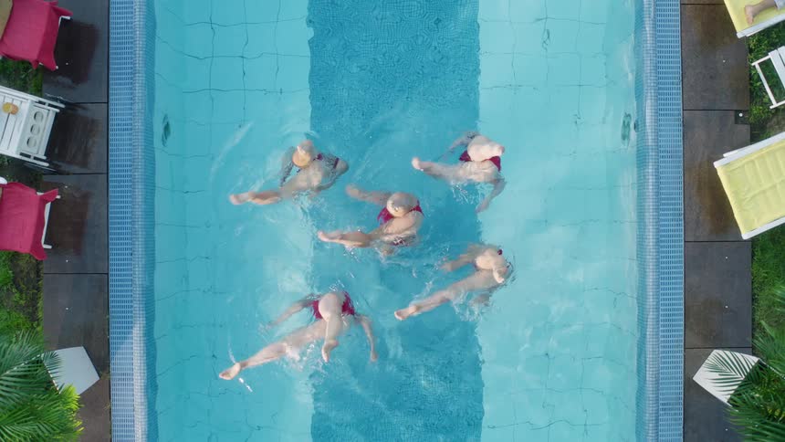 Five women synchronize swim in an outdoor pool