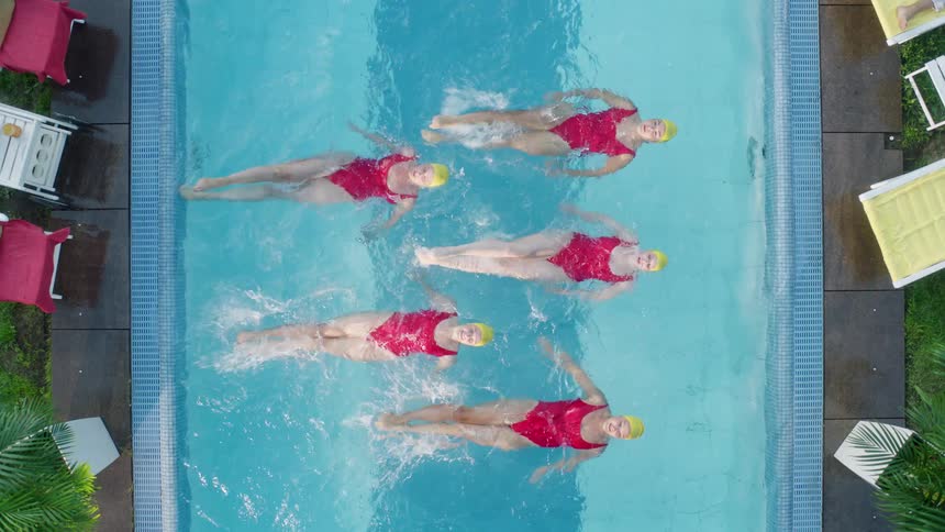 Five white women synchronize swim in an outdoor pool